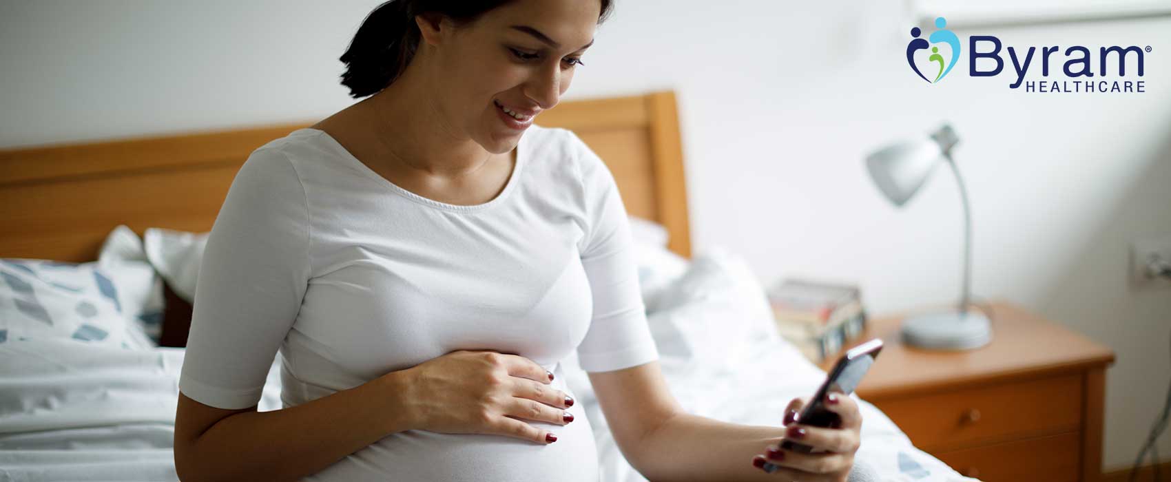 Embarazada mirando un teléfono y sonriendo.