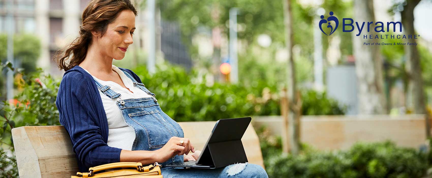 Embarazada sentada en un banco con su computadora portátil.