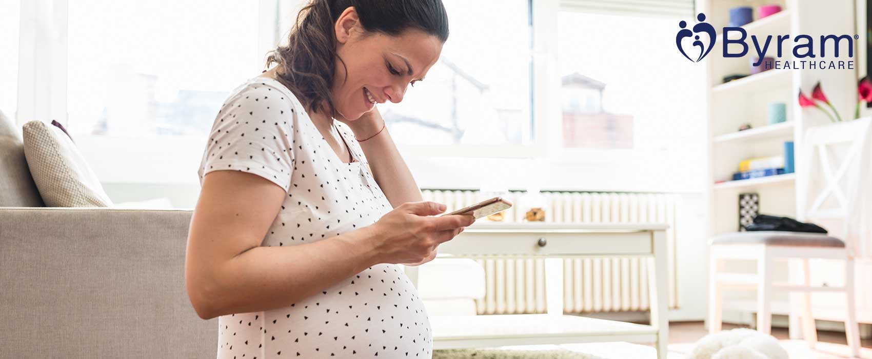 Pregnant lady looking at Elvie breast pumps on her phone, smiling.