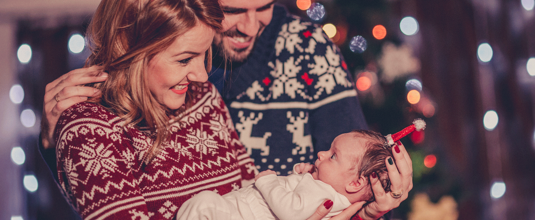 parents hold newborn in holiday sweaters